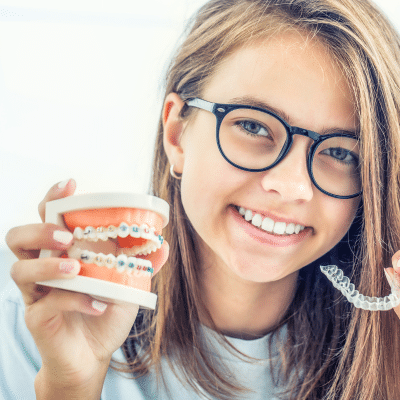 Young girl smiling holding aligners and plastic teeth