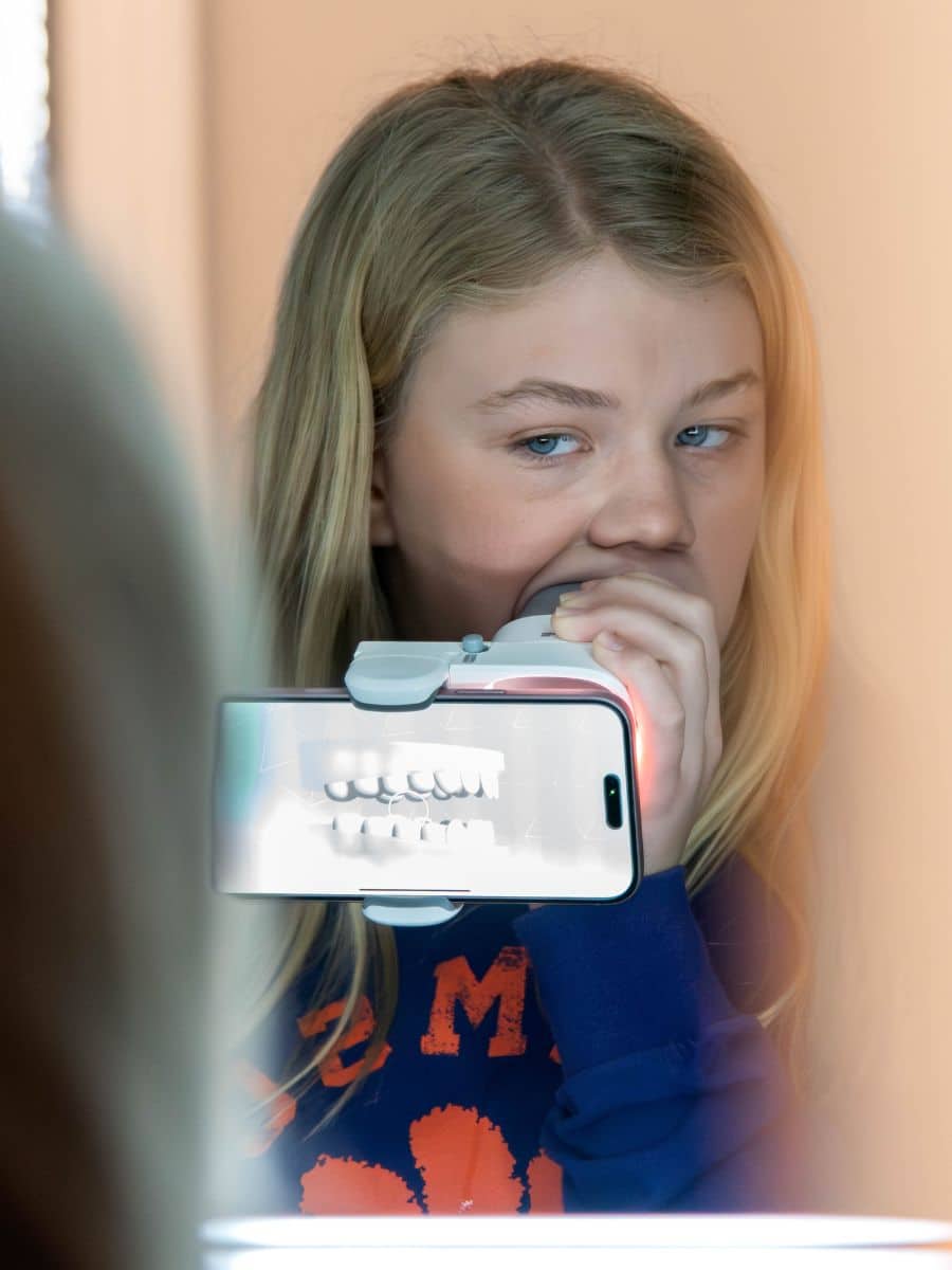 On the go with grosso 3 Girl using a digital tool to examine her teeth during a virtual consultation with grosso orthodontics in south carolina